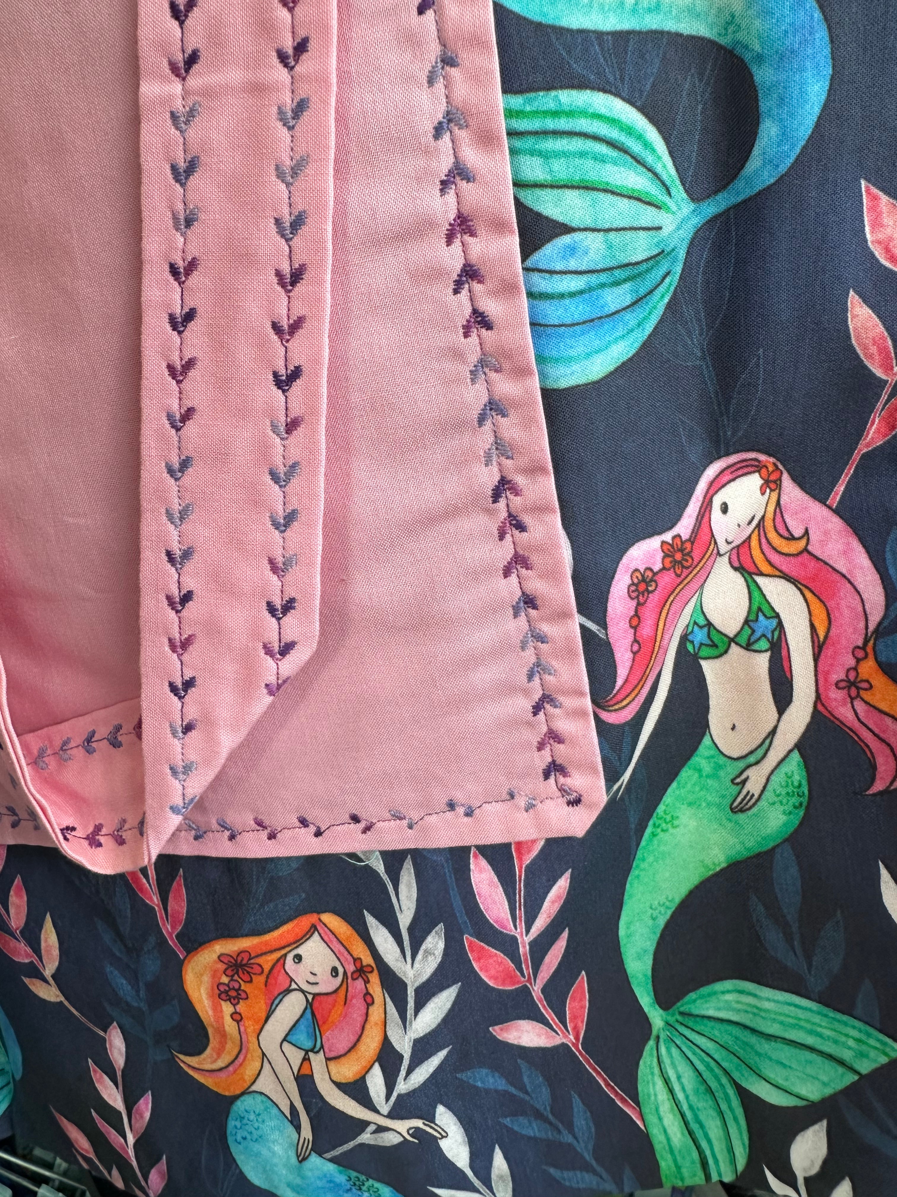 Pink fabric with embroidered stitching on a colorful mermaid-patterned background