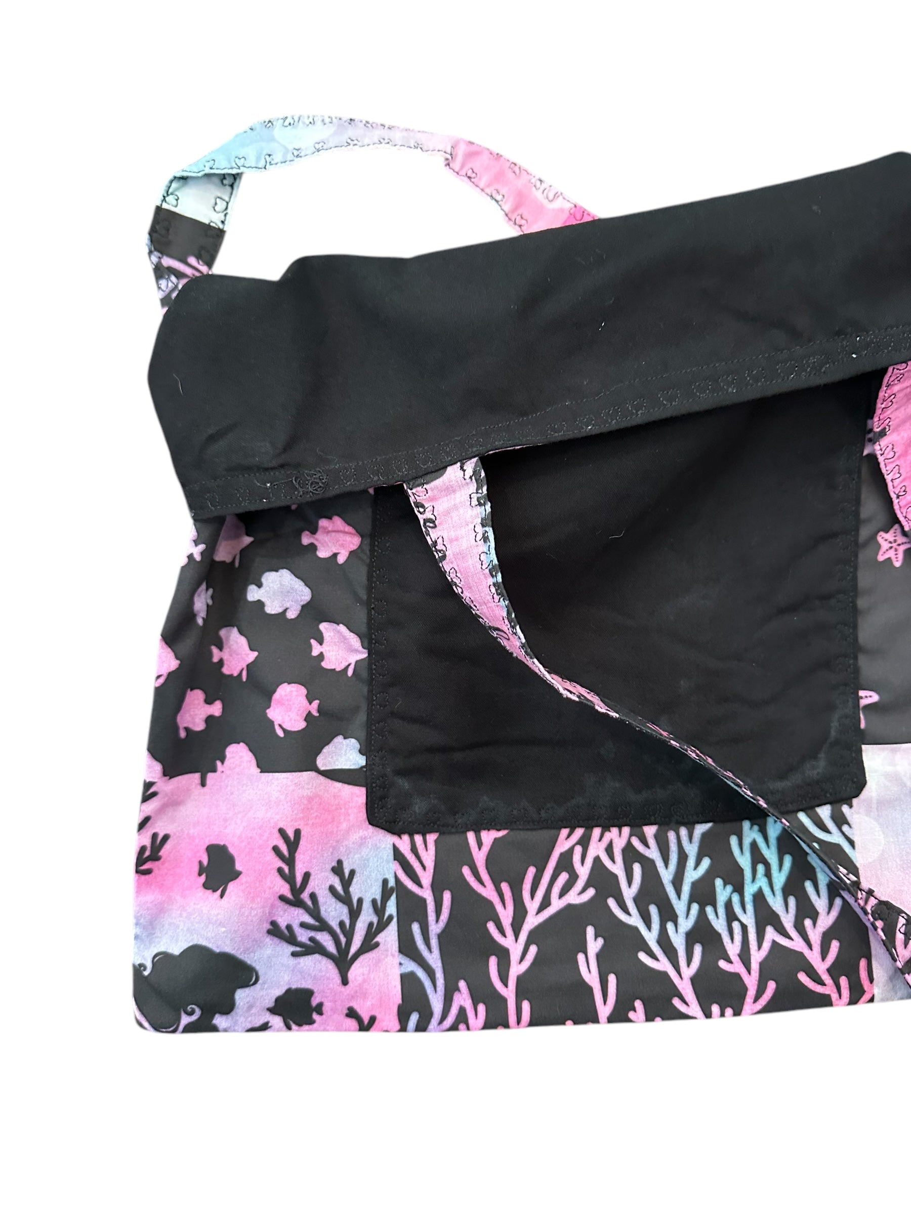 Close-up of a black bag with pink and blue coral and fish pattern on a white background