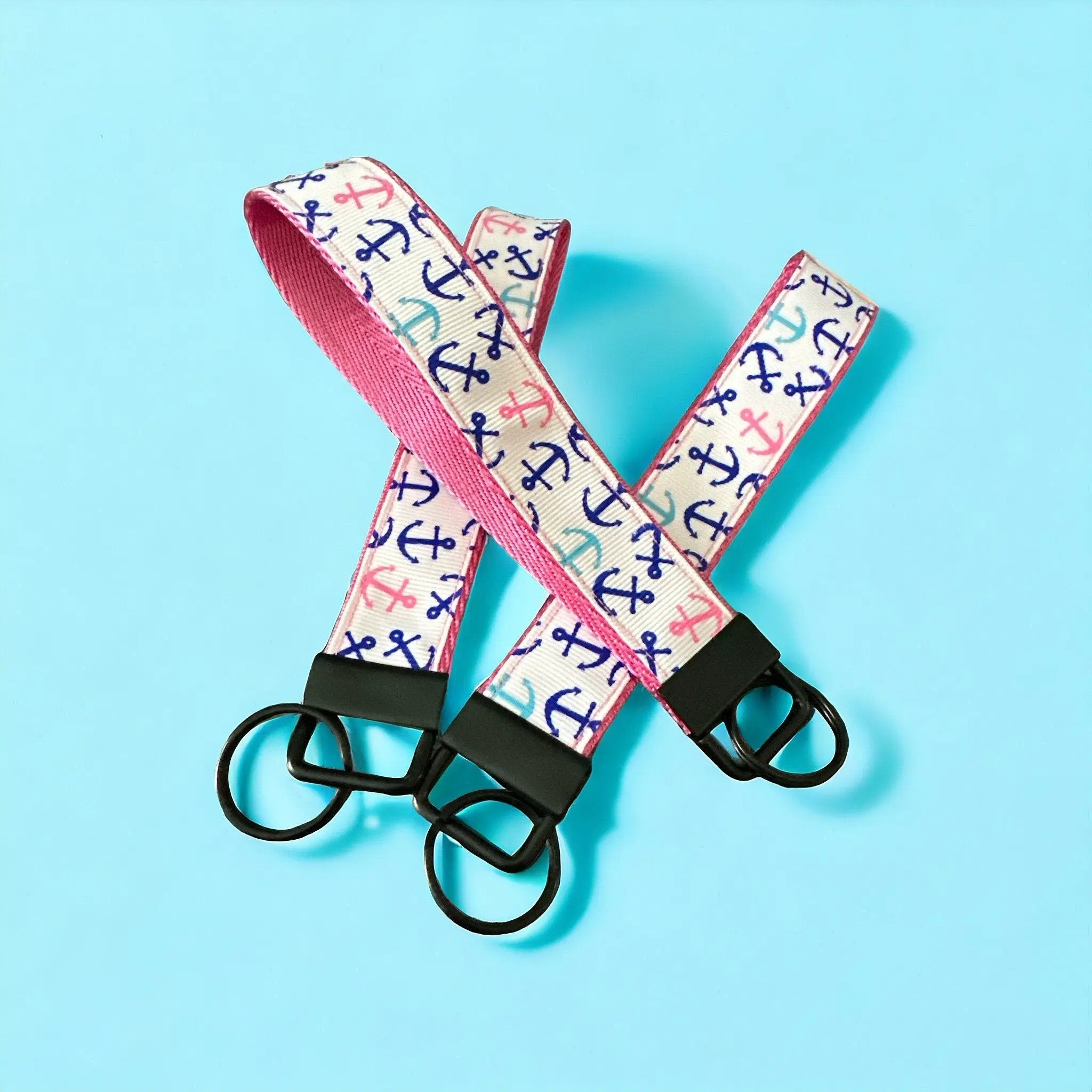Two pink lanyards with anchor pattern and black key holders on a light blue background
