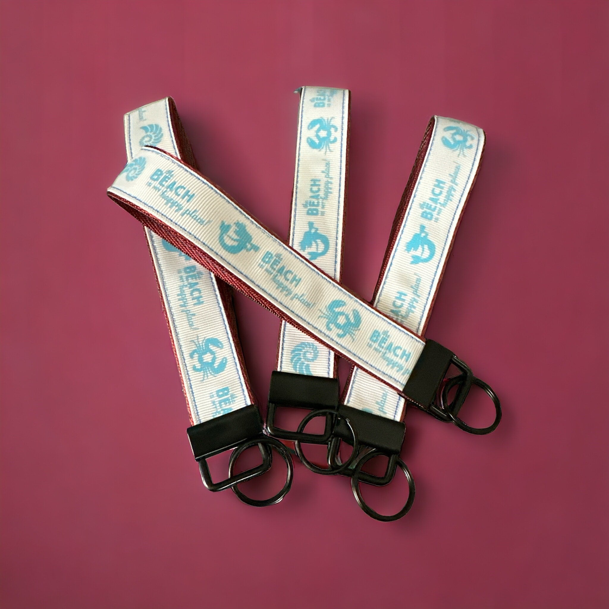 Set of three keychains with striped bands and black clasps on a purple background