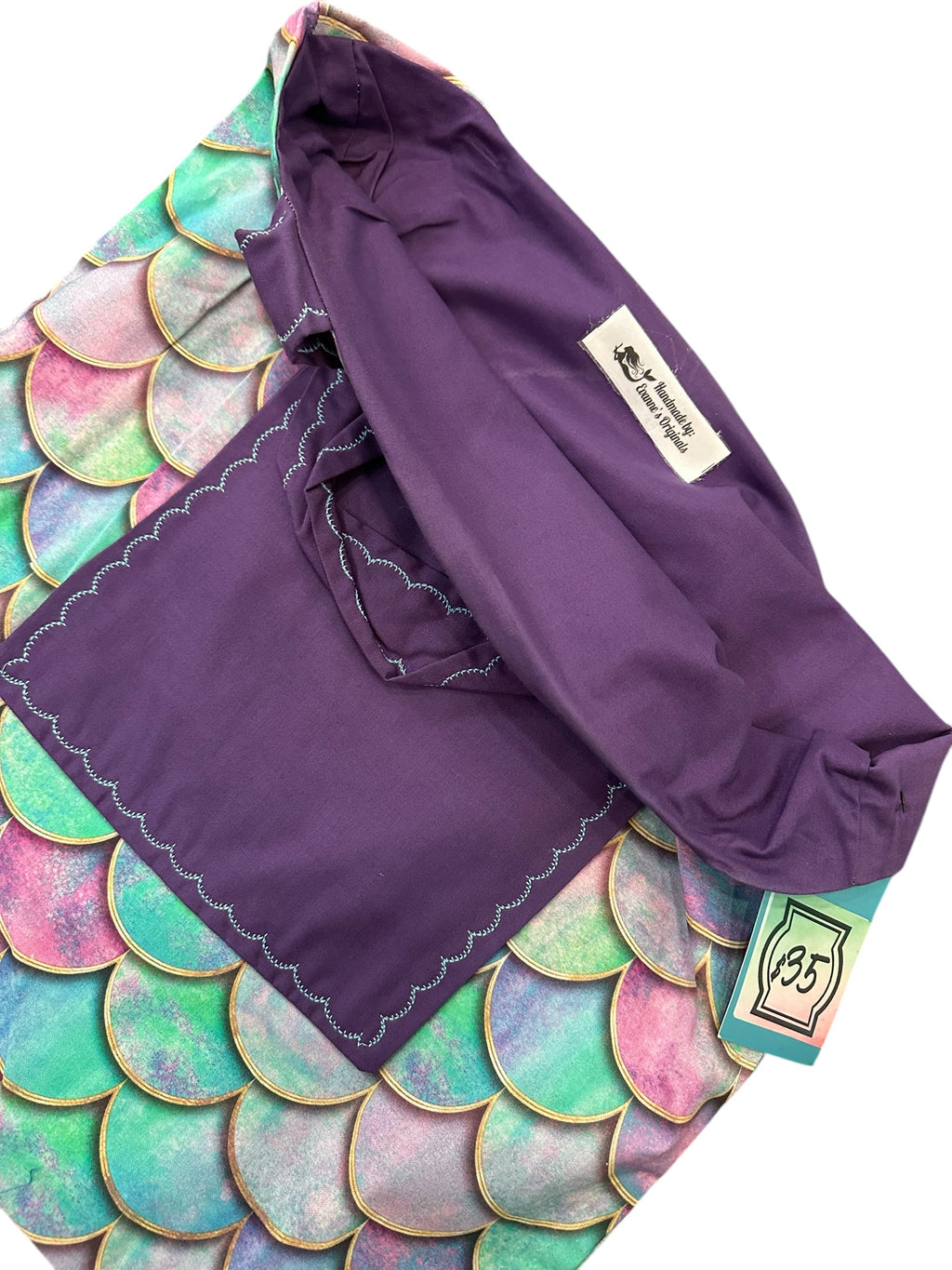 Purple garment with a brand label on a colorful mermaid scale pattern